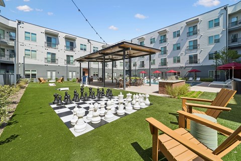 A giant chess board is set up on a lawn in front of apartment buildings.