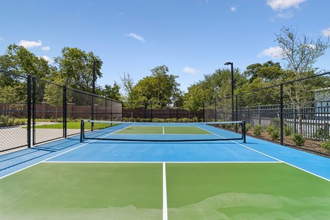 A tennis court with a blue and green surface surrounded by a black fence.