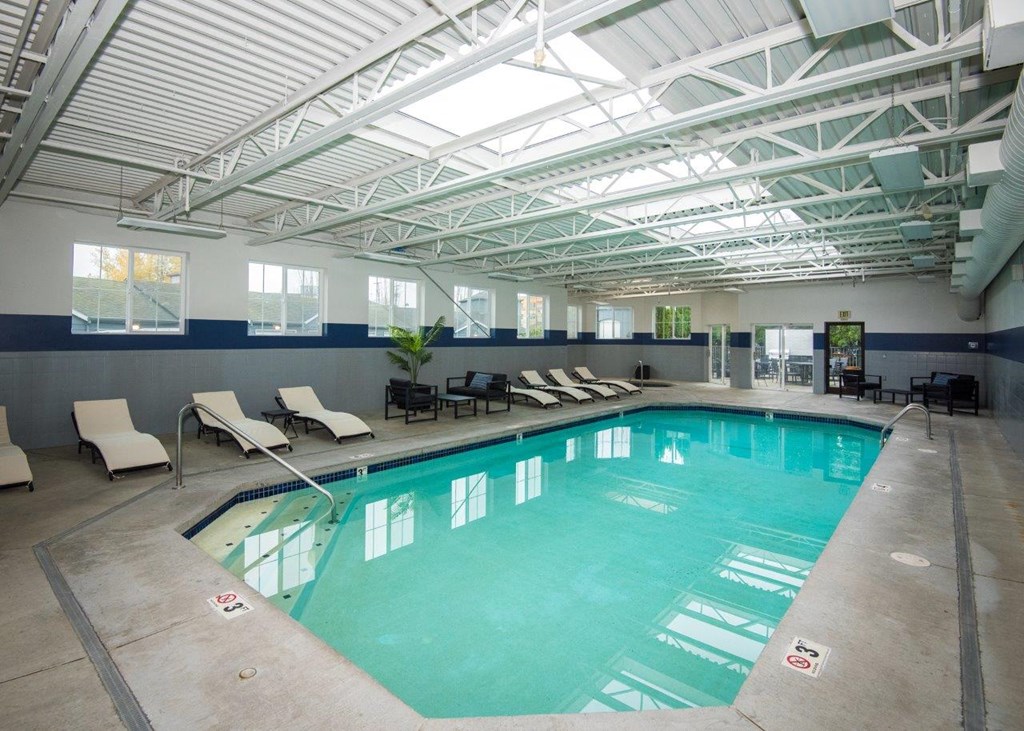 a large indoor swimming pool with chaise lounge chairs and a ceiling with skylights