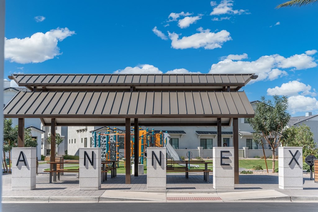 A playground with a slide and a bench under a roof with the letters ANNEX on it.