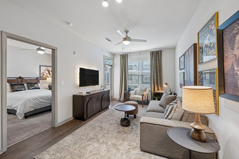 A well-lit, modern bedroom with a large bed, a flat-screen TV, and a seating area.