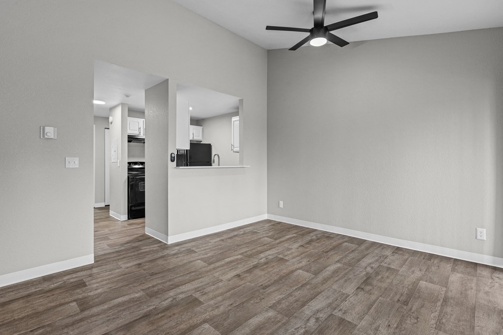 an empty living room with a ceiling fan and a kitchen