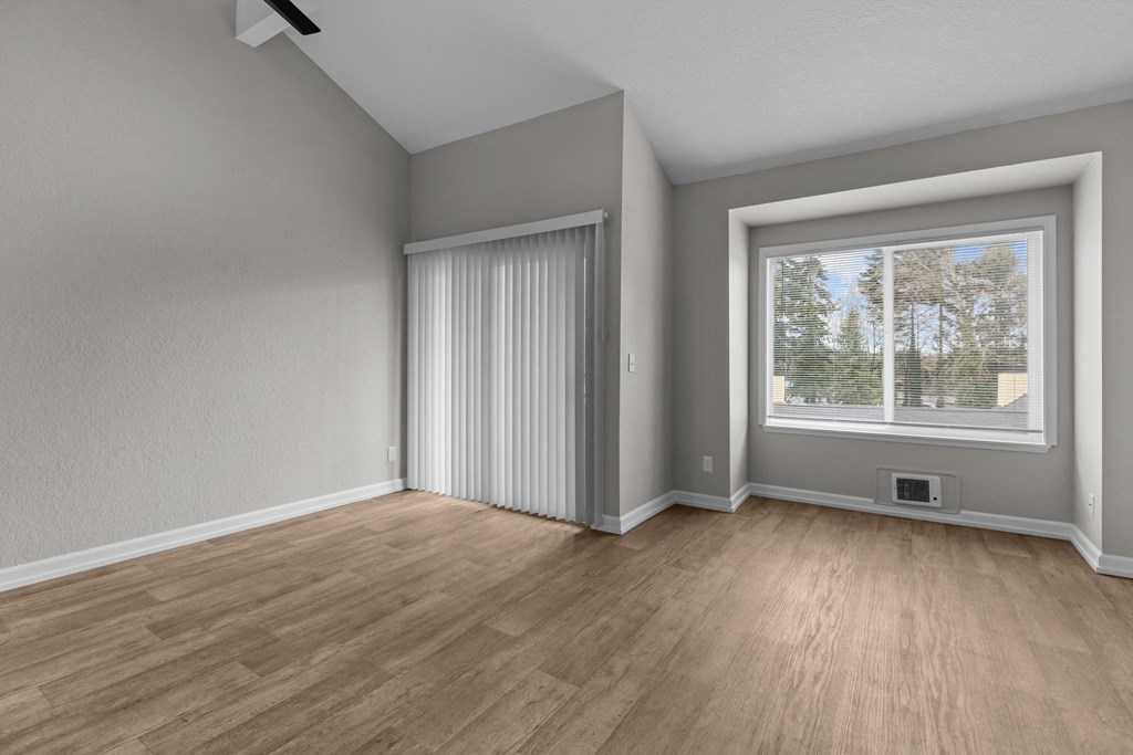 an empty living room with a large window and wood flooring
