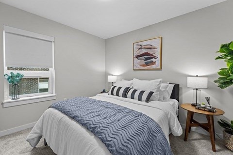 A bedroom with a large bed and a small table with a lamp on it.