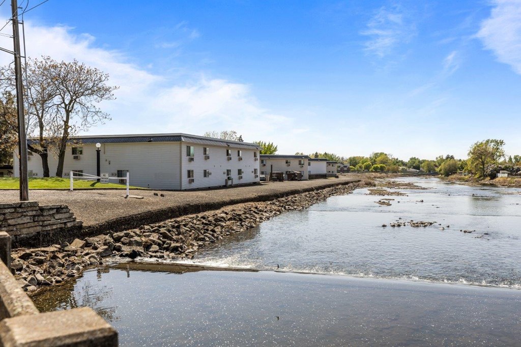A white building is situated by a body of water with a rocky shore.
