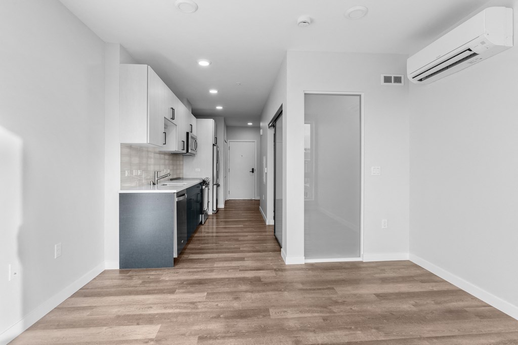 a renovated apartment with white walls and wood flooring and a kitchen