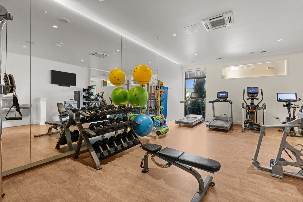 a gym with cardio equipment and weights on a wooden floor