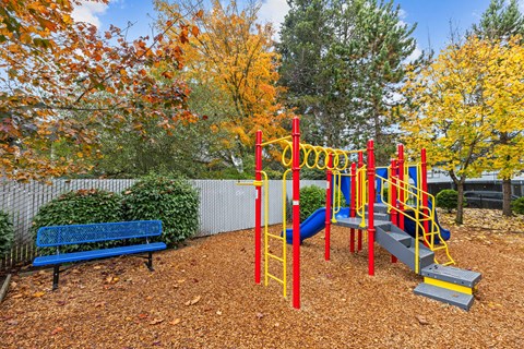 A playground with a red and yellow swing set and a blue bench.