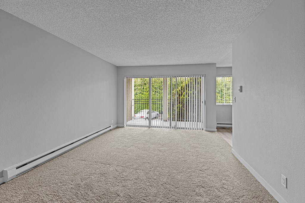 an empty living room with a sliding glass door to a balcony