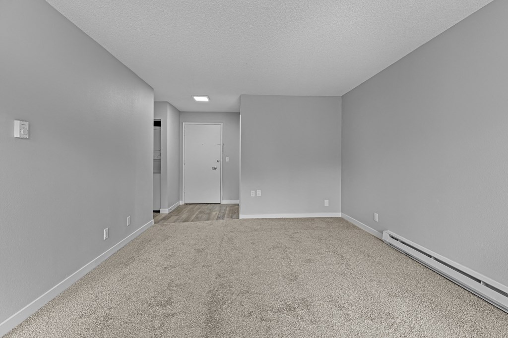an empty living room with carpet and a door to a bedroom