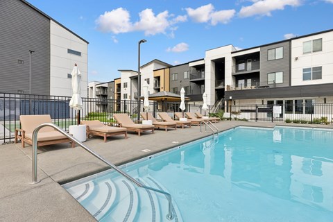 A swimming pool with sun loungers and apartment buildings in the background.