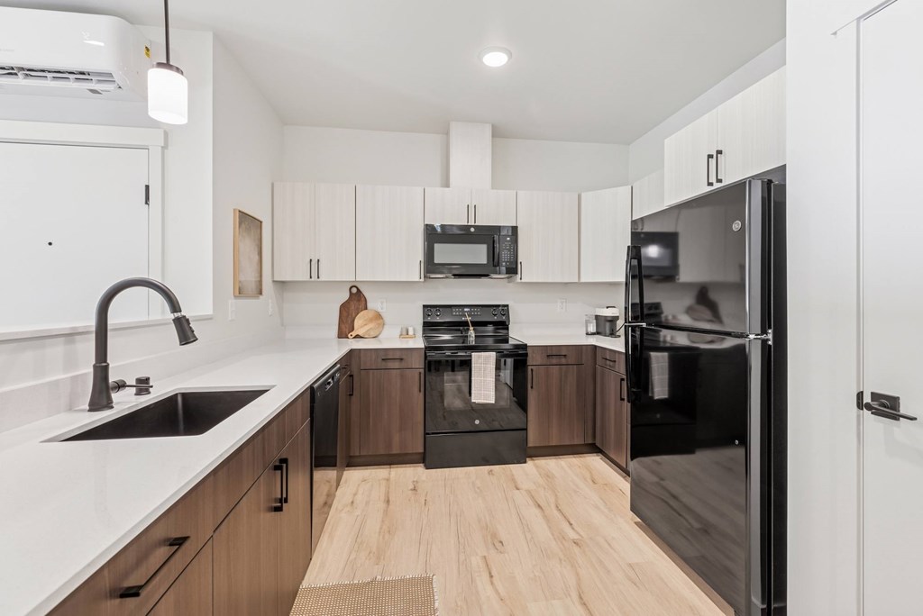 A modern kitchen with a black refrigerator and wooden floors.