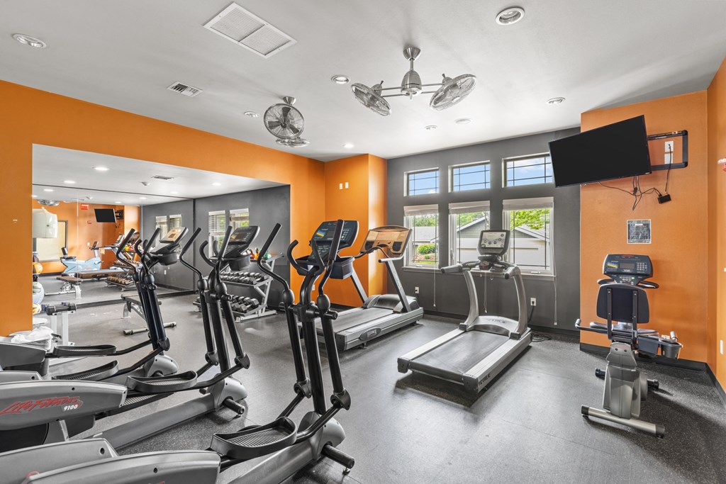 a gym with cardio equipment and a flat screen tv