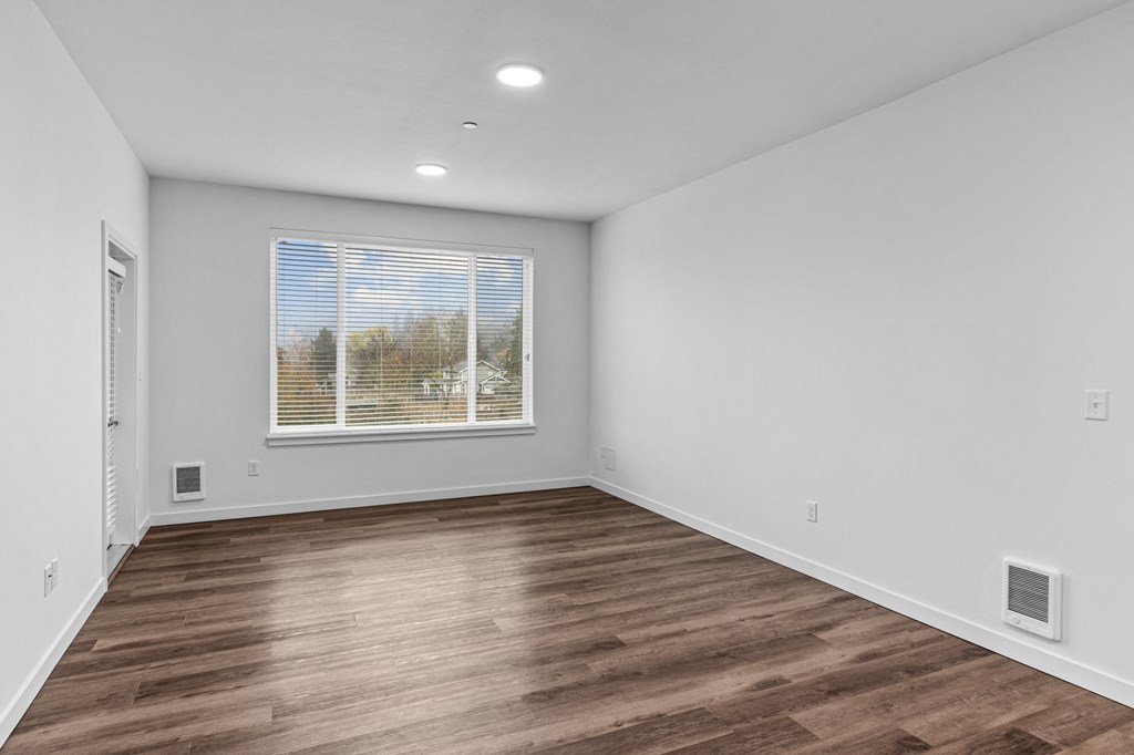 a living room with white walls and wood flooring and a window