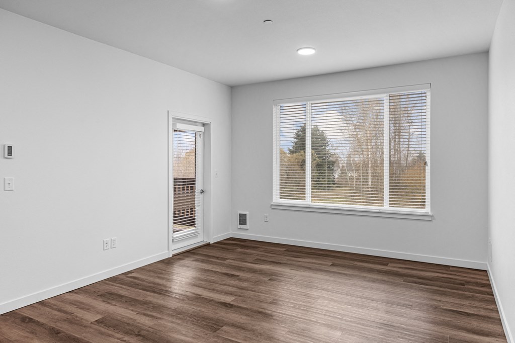 the living room of an apartment with a large window and wood flooring