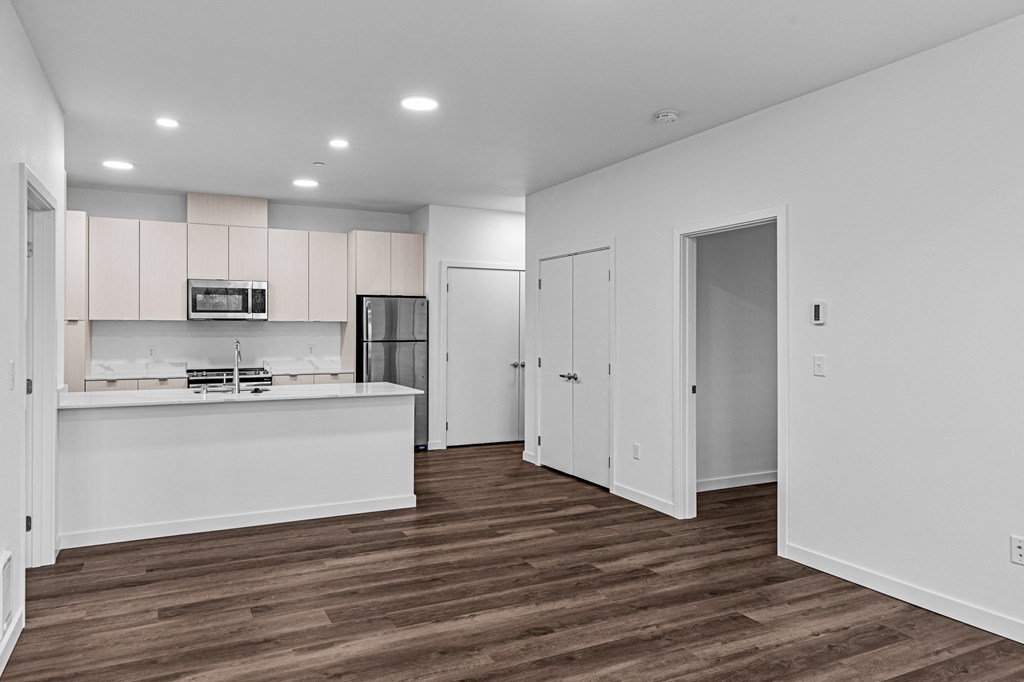 an empty living room and kitchen with white walls and wood flooring