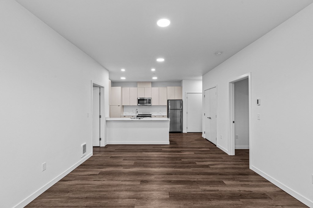 the living room and kitchen of a new home with white walls and wood floors