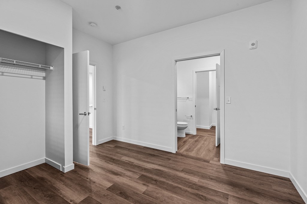 a bedroom with white walls and a bathroom with a toilet and a closet