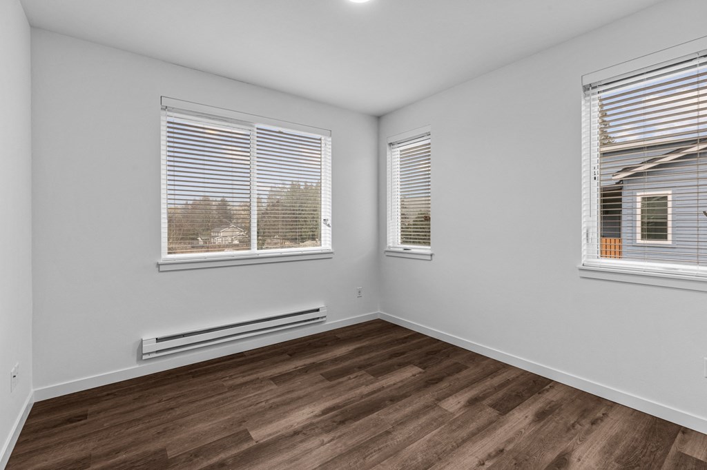 the living room of an apartment with wood flooring and three windows