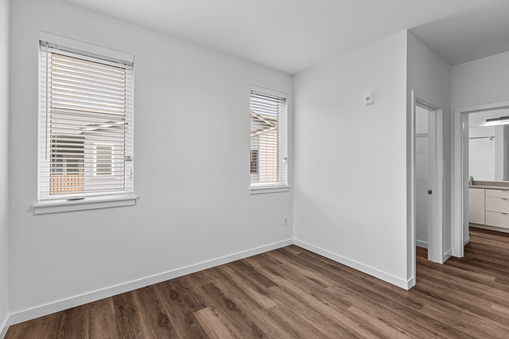 the living room of an apartment with white walls and wood flooring