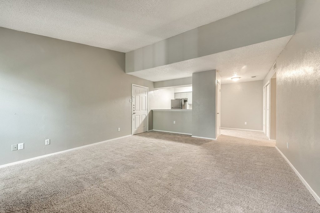 the spacious living room and dining room of an apartment with carpeting and a kitchen