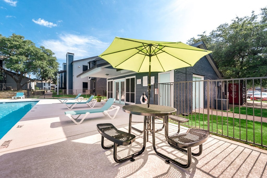 our apartments have a large pool and a patio with chairs and an umbrella