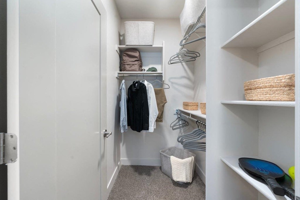 a small walk in closet with shelves and a closet door open to a white closet