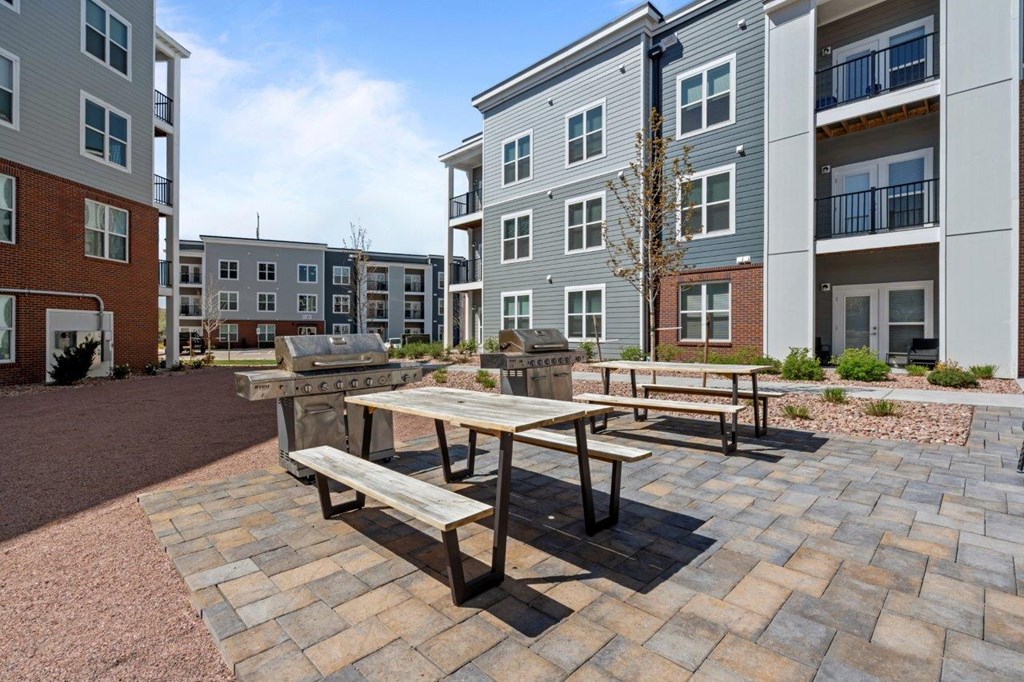 A wooden table and benches are set up in a courtyard with brick pavers.
