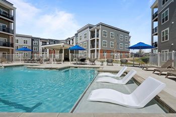 A pool area with white lounge chairs and a blue umbrella.