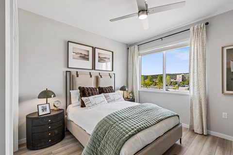 A bedroom with a large bed, a ceiling fan, and a view of the outdoors through a window.