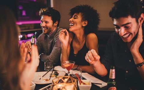 a group of people sitting at a table eating and laughing at a restaurant