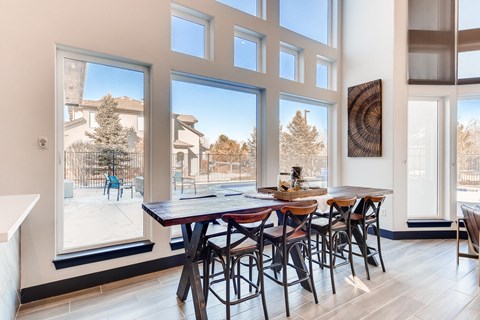 A dining room with a table and chairs in front of large windows.