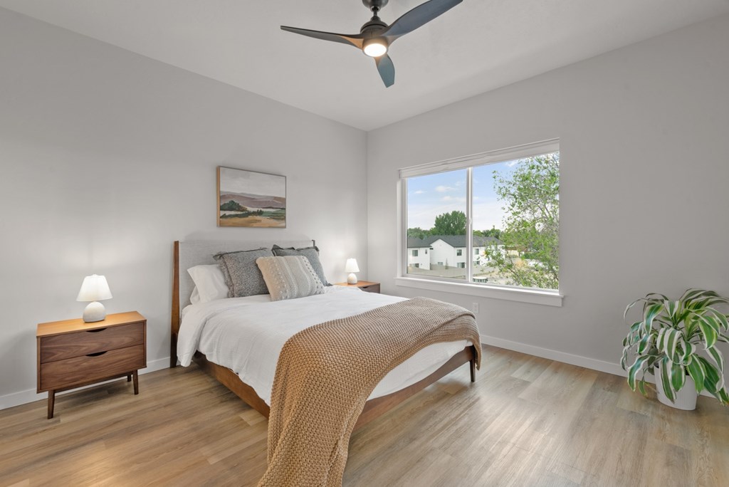 A bedroom with a bed, nightstand, and a potted plant.