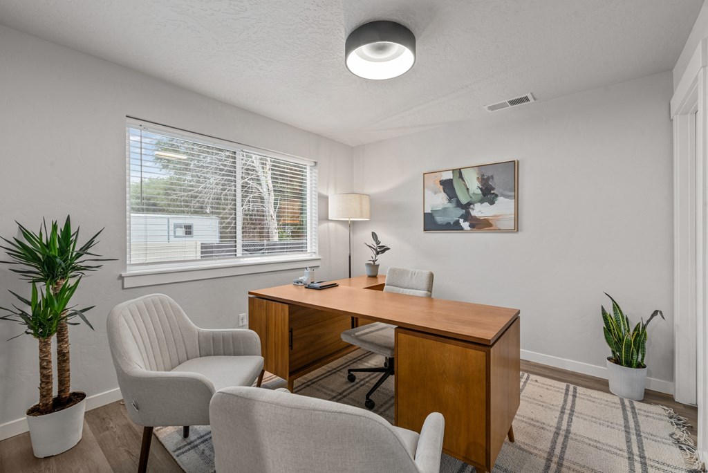 A room with a desk, chairs, and plants.
