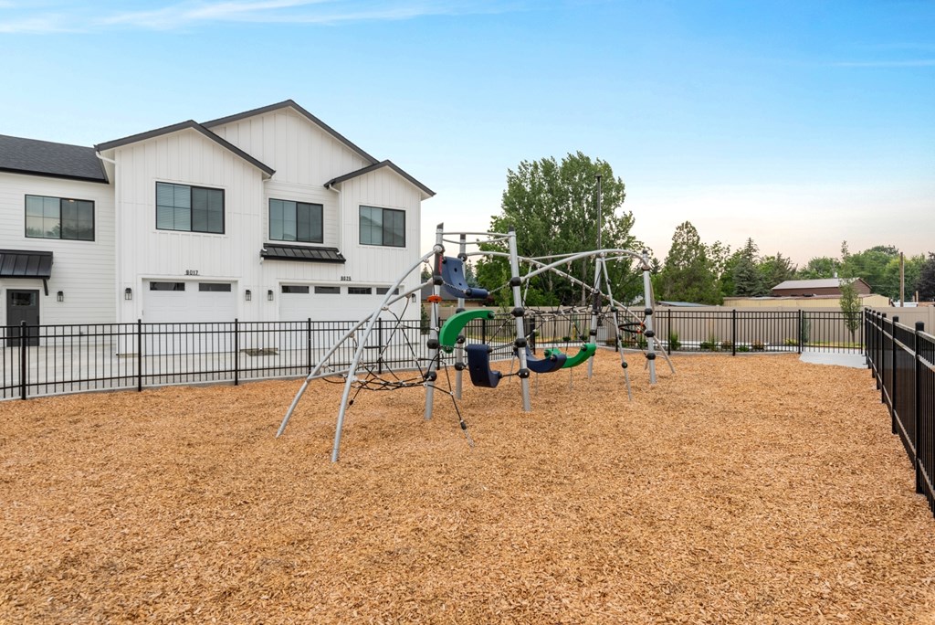 A playground with a swing set and a slide in front of a white house.
