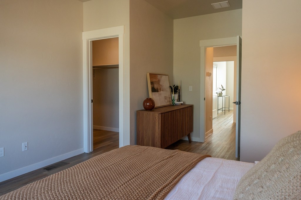 A bedroom with a bed, a wooden dresser, and a doorway leading to another room.