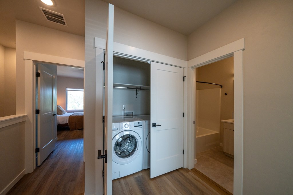 A view of a bedroom, a washing machine, and a bathroom from an open door.
