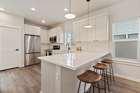 A kitchen with white cabinets and a white island with three stools.