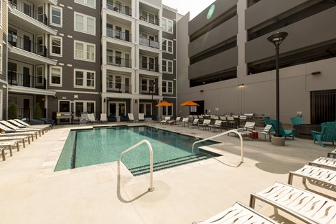 A swimming pool in front of a building with lounge chairs around it.