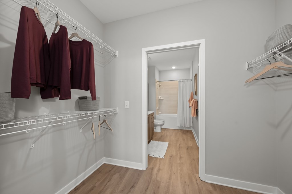 A white closet with clothes hanging and a mirror on the wall.
