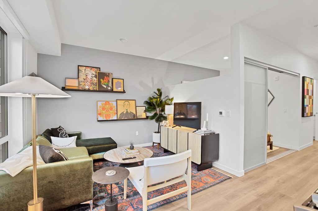 A living room with a green couch, a white chair, a white coffee table, a lamp, a TV, and a painting on the wall.