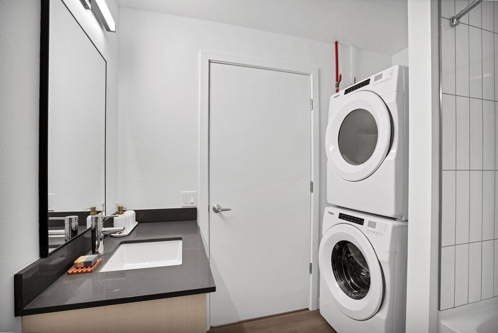 A white door is open to a bathroom with a washer and dryer stacked on top of each other.