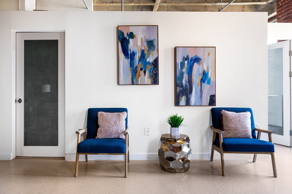 a living room with two blue chairs and paintings on the wall