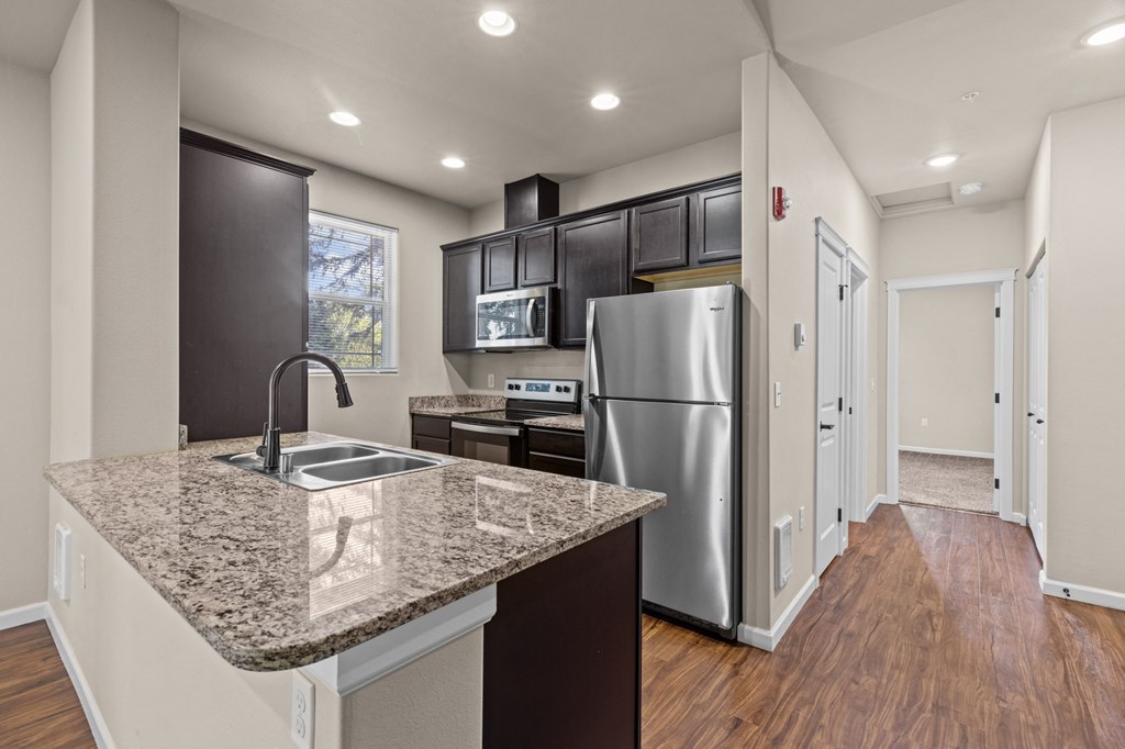 Little Tuscany Apartments & Townhomes - Kitchen with Dark Cabinets, Granite Countertops, Vinyl Wood Planking, White Door and Floor Trim, Stainless Steel Cabinets