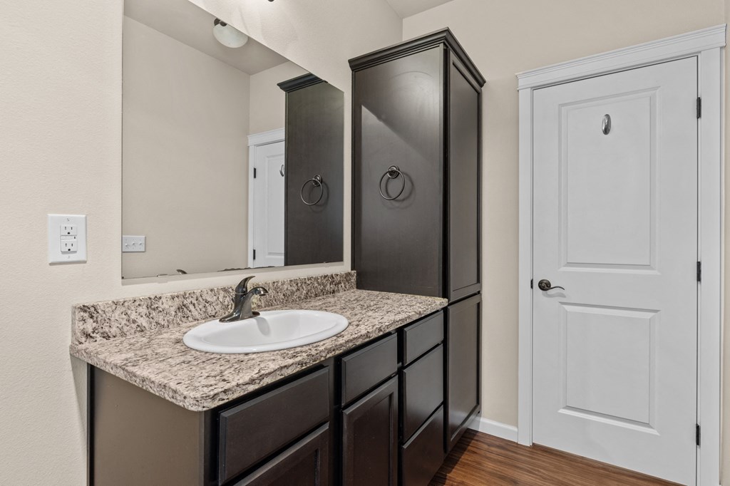 Little Tuscany Apartments & Townhomes - Apartment Bathroom with Dark Cabinets, Granite Countertops, Wood Plank Flooring, White Woodwork