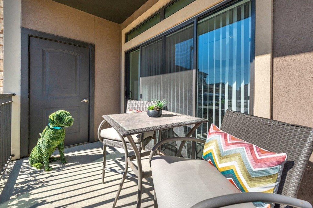 a dog sitting on a balcony with a table and chairs
