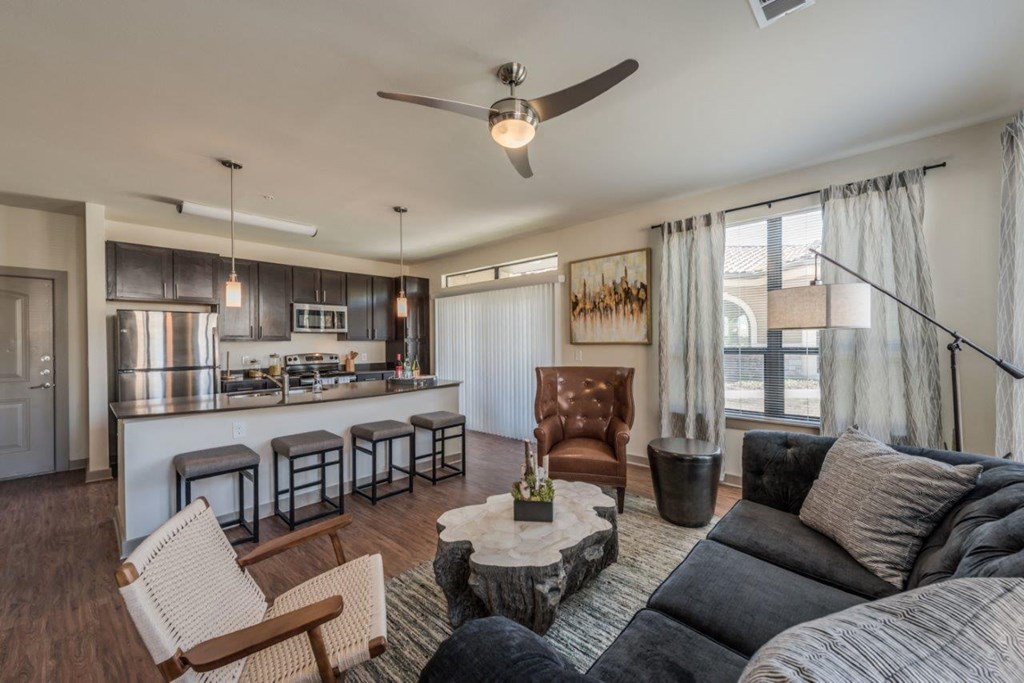 a living room with a couch and a chair in front of a kitchen with a breakfast bar