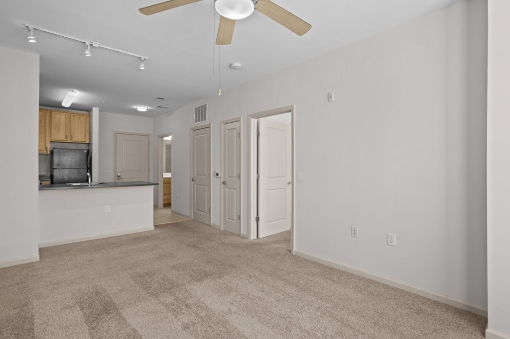 A spacious living room with a ceiling fan and carpeted floor.