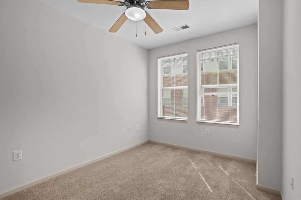 A room with a ceiling fan and two windows.