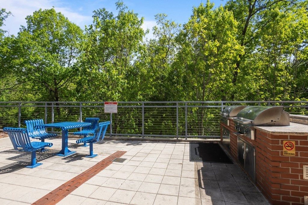 A blue table and chairs are on a patio with a brick wall and a trash can.
